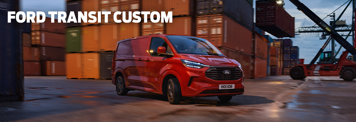 Ein roter Ford Transit Custom fährt durch einen Containerhof bei Dämmerung.